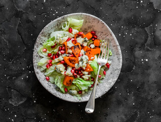 Delicious seasonal salad with pumpkin, gorgonzola, pomegranate, iceberg on a dark background, top view