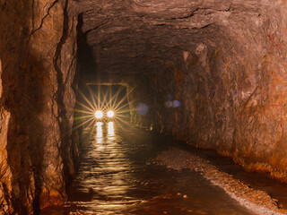 coming car lights from inside deep old mining tunnel cave with reflection. rock wall cave with...