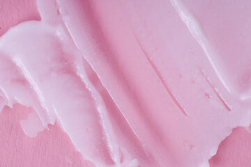 Smeared textured cream on a pink background. Macro shot of a creamy texture. 