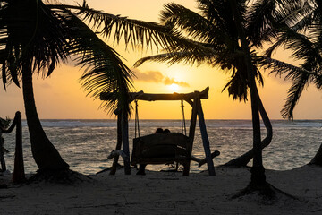 Romantic sunset, Caribbean postcard, couple watching the ocean on wooden swing, relax concept, backlight silhouettes