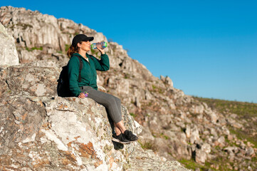 young woman on top of a mountain appreciating the landscape on a sunny day relaxed with her backpack and water enjoying