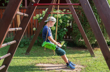Fototapeta premium boy swinging on a swing in the summer village