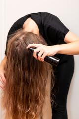 Young woman hand holds bottle and spraying her wavy blond long hair. Hair protection and treatment...