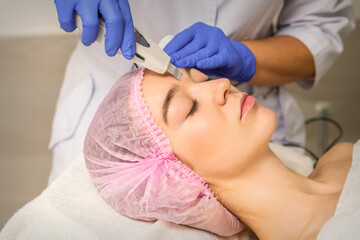 Naklejka premium Young caucasian woman having ultrasonic peeling with ultrasound device in a cosmetic beauty salon