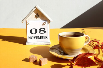 Calendar for November 8: a cup of tea with branches of girlish grapes against the background of a decorative house with the name of the month in English and the numbers 08, gray background