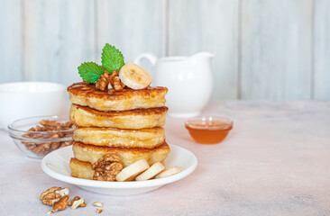 Homemade pancakes with nuts, honey and banana on a light background.