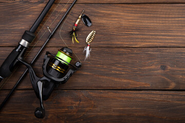 Fishing tackle - fishing spinning rod, hooks and lures on wooden background. Active hobby recreation concept.