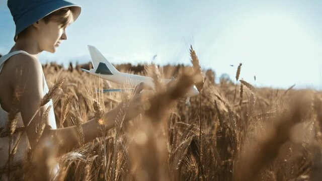 cinematic boy in a hat playing with airplane in the golden wheat field, moving camera