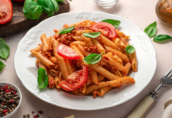 Penne pasta with tomato sauce and fresh tomatoes on a light background.