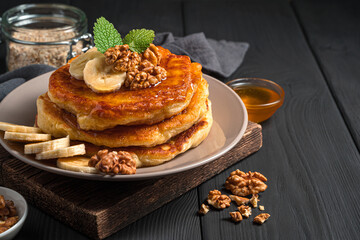 Homemade pancakes with banana, honey and nuts on a black background.