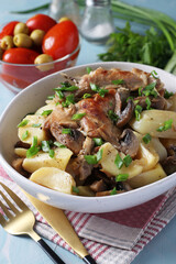 Rabbit meat with potatoes and mushrooms in a light plate on a light blue background.