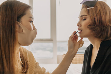 Asian woman makeup artist is at work and wearing makeup on her model.