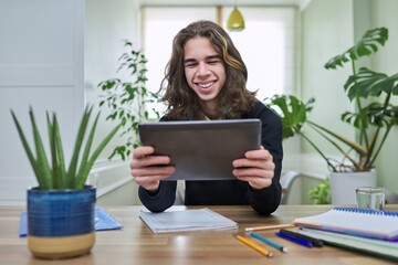 Virtual online lesson, smiling teenager guy learns remotely using digital tablet