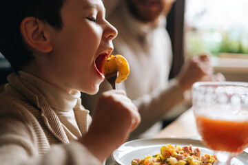 Close-up face of pretty child kid boy eating fried potatoes sitting at dinner feast table during...