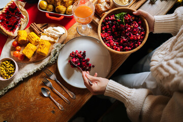 Close-up top view of unrecognizable young woman putting salad on plate preparing Christmas table at home for family party in cozy dinner room. Female serving beautiful table for friendly feast