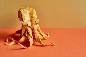 Origami octopus model on a yellow and orange background. Origami figure on a paper texture surface....