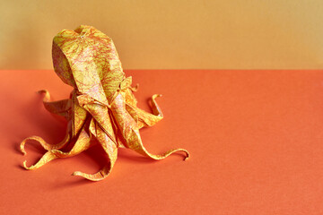 Origami octopus model on a yellow and orange background. Origami figure on a paper texture surface....