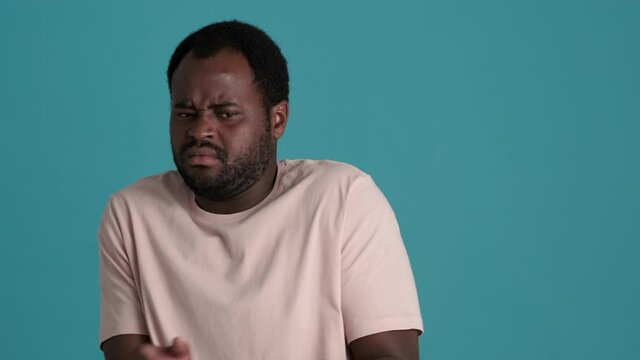 Displeased African man wearing t-shirt showing gesture of disgust and waving hands in blue studio