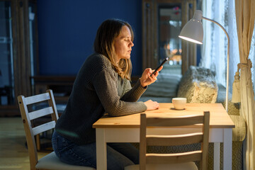 Woman in sweater using her phone sitting near wooden table at home living room