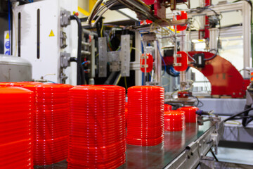 Factory machine placing red plastic lids on conveyor belt. Industrial technology for food containers, manufacture concepts