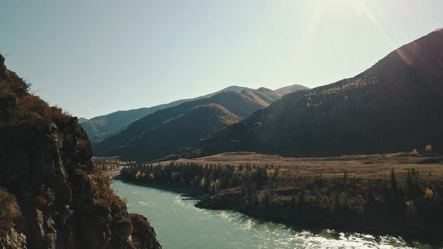 Aerial view of the calm mountain river Katun. Autumn landscape of the wild nature of the Altai Territory: Mountains, forests, fields, a country walking road, the rays of the sun. The camera flies
