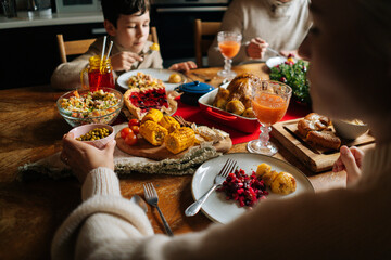 View from back of Caucasian young family enjoying at festive Christmas table during holiday family party. Cheerful mother, father and little son having dinner xmas party, eating and chatting at home.