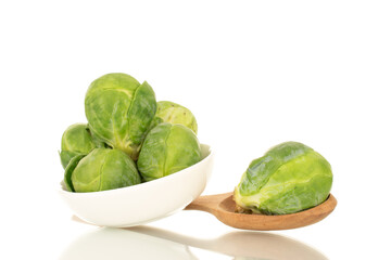 Organic ripe brussels sprouts with white saucer and wooden spoon, close-up, isolated on white.