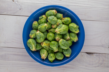 Organic ripe Brussels sprouts in a ceramic dish on a wooden table, close-up, top view.