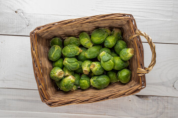 Organic ripe Brussels sprouts in a basket on a wooden table, close-up, top view.