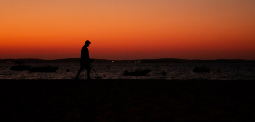 silhouette d'une personne et d'un détecteur de métaux pendant un coucher de soleil à la mer 