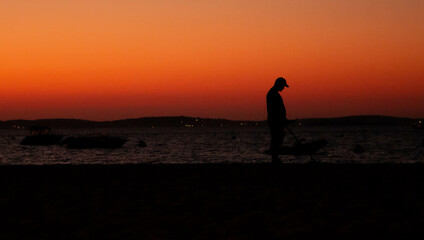Plakat silhouette d'une personne et d'un détecteur de métaux pendant un coucher de soleil à la mer 