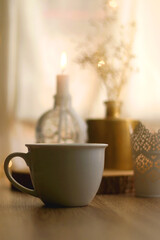Obraz na płótnie Canvas Cup of warm drink, lit candles and flowers on a table. Hygge at home. Selective focus.