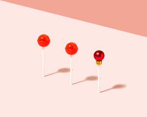 Creative composition with tasty red lollipops and Christmas bauble against pastel pink background.  Minimal xmas candy concept.