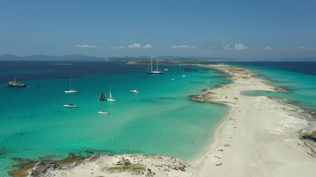 Illetes beach in Formentera, turquoise waters and white sand. Boats and yachts moored off its shores in summer. Drone footage.
