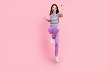 Photo of lucky pretty young lady wear striped outfit smiling jumping high rising fists isolated pink color background