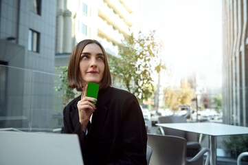 Attractive pensive brunette woman holding a credit card with green chroma key for ads, looking...