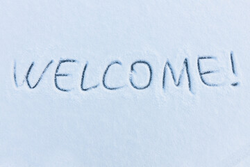 Handwritten word welcome on a snowy surface. Winter holidays concept background.