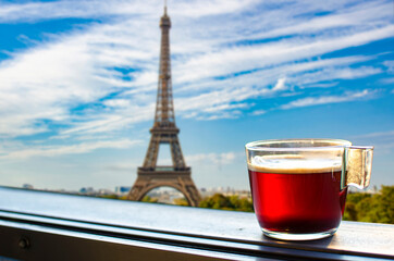 Glass cup of coffee or tea on balcony with view on Eiffel tower and Paris skyline background. Sunny view of glass of tea overlooking the Eiffel Tower in Paris, France