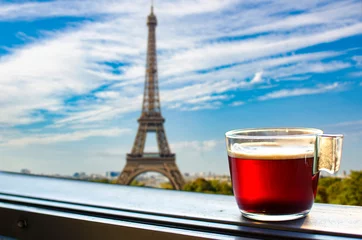  Glass cup of coffee or tea on balcony with view on Eiffel tower and Paris skyline background. Sunny view of glass of tea overlooking the Eiffel Tower in Paris, France © Maria Vonotna