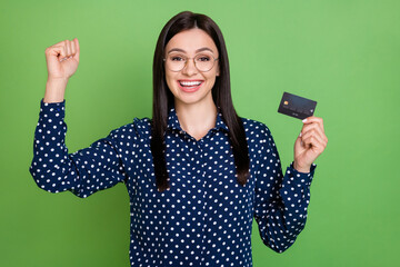 Photo of astonished girl hold credit card celebrate jackpot wear specs dotted blouse isolated on green color background