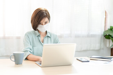 Beautiful Asian businesswoman in wears medical protective mask sit at table at home using laptop computer. Self-isolation quarantine. Social Distancing At Work During Coronavirus Covid-19 Pandemic