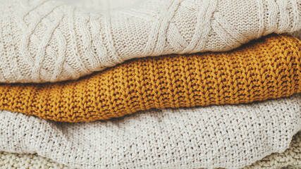 Cozy knitted sweater background. Pile of white, yellow and beige knit sweaters close up. Hello...