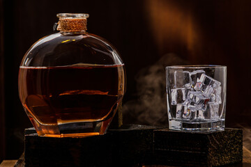 black wooden table, bottle and glass of whiskey with ice.