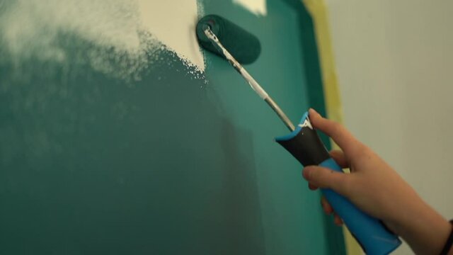 Closeup the hand of young teen girl paints a white wall teal color. Renovation and creativity concept. Finishing tools