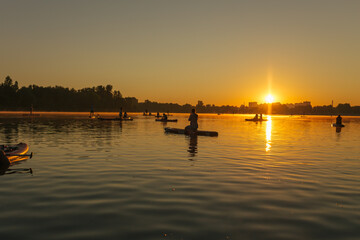 Silhouettes of a people on a sup on the background of the river in the rays of the sunset