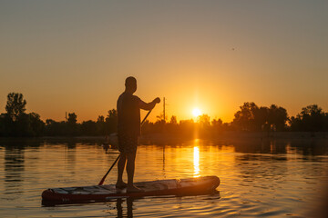 Silhouette of a man on a sup on the background of the river in the rays of the sunset