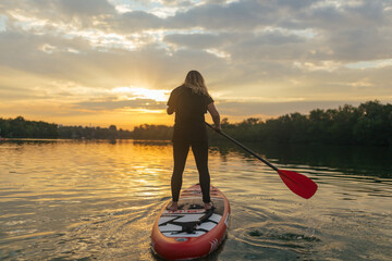 SUP silhouette of young girl paddle boarding at sunset