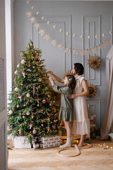 Mother and daughter decorate the Christmas tree together. Stylish interior of a children's room. Scandinavian eco-style decor. New Year celebration. Christmas eve. Support joint time forwarding. love