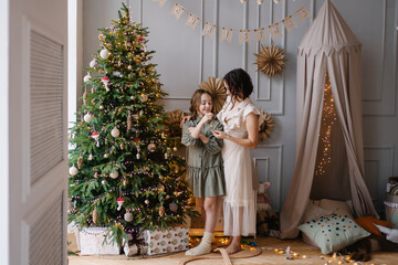 Mother and daughter decorate the Christmas tree together. Stylish interior of a children's room. Scandinavian eco-style decor. New Year celebration. Christmas eve. Support joint time forwarding. love