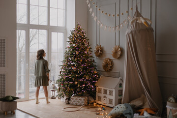 A 10-year-old girl stands at the window in the children's room and waits for santa claus. Christmas...